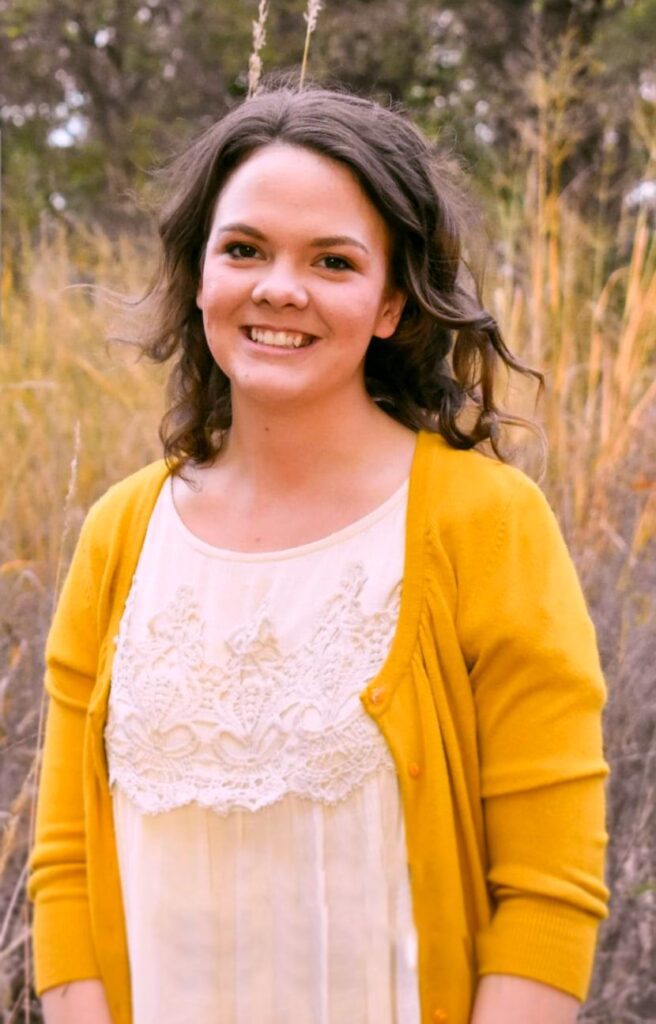 A woman in yellow jacket standing next to tall grass.